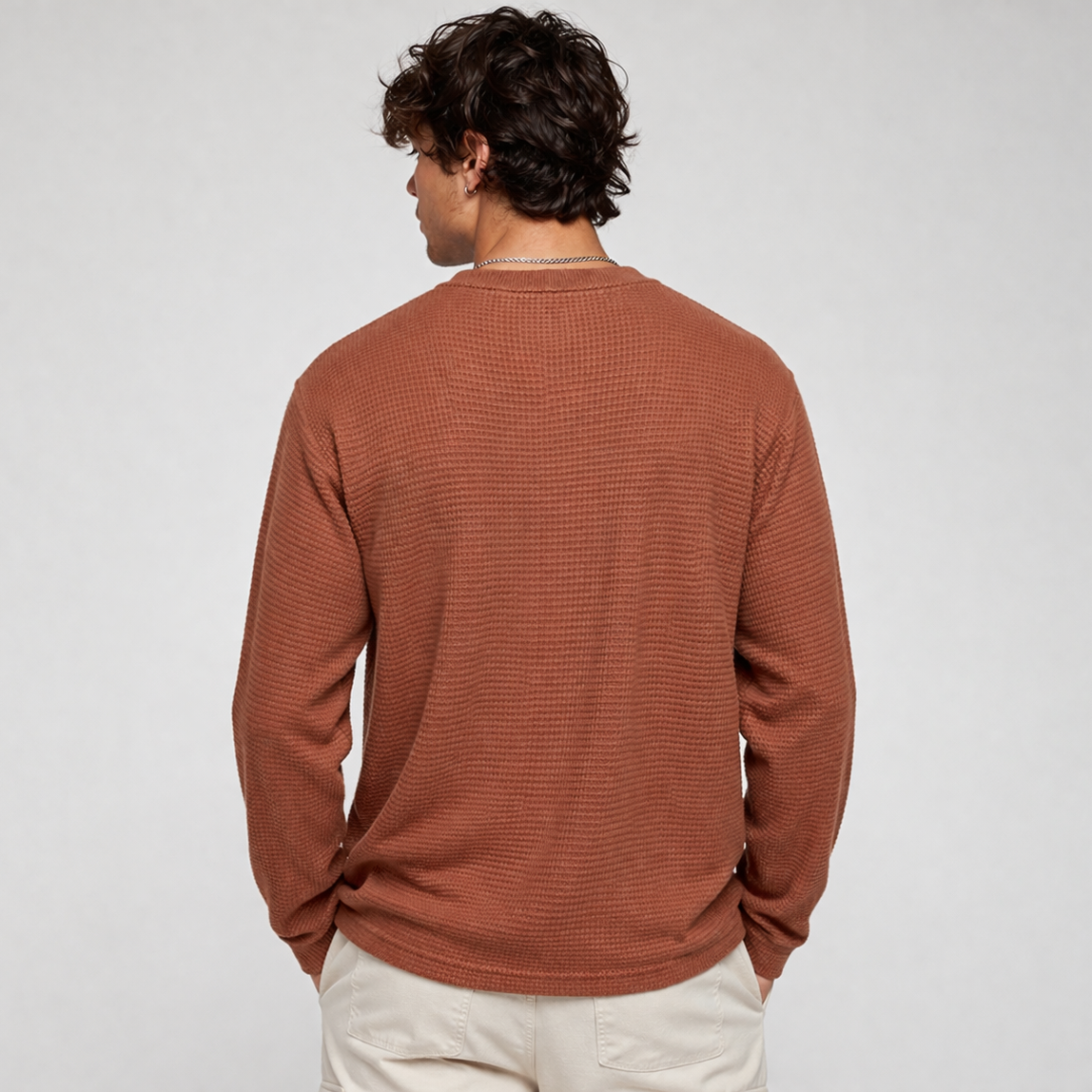 Man wearing a brown sweater and beige pants on a white background
